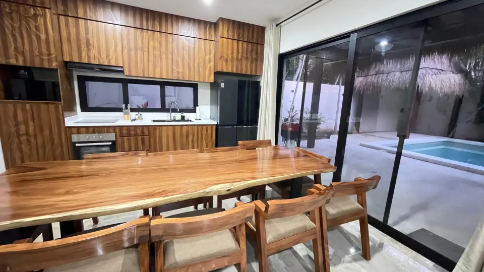 A long wooden dining table in the villa, with the private pool beyond the glass doors.