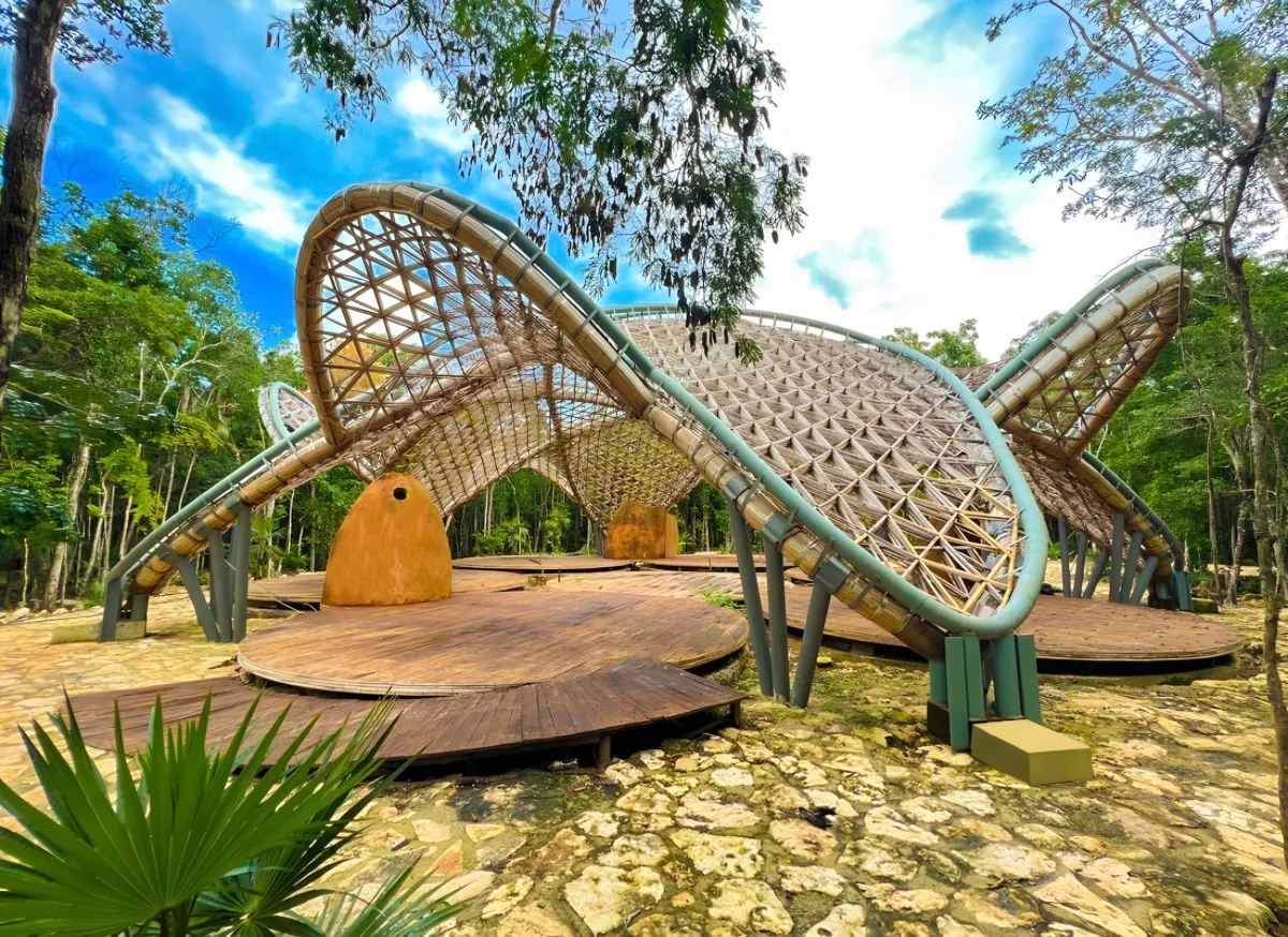Woven bamboo pavilions with petal-shaped roofs on a stone platform in the jungle.